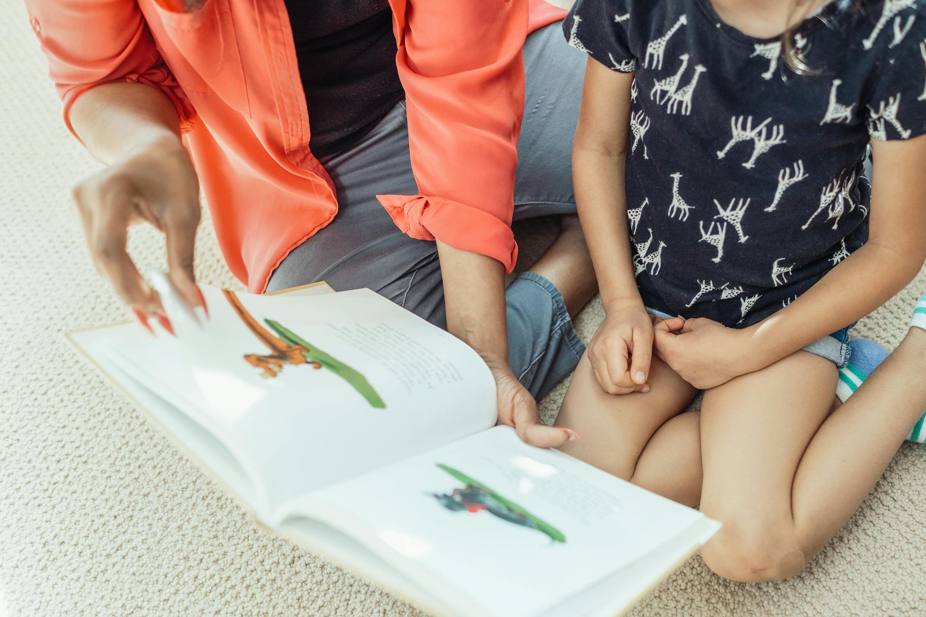 A mother and daughter sit on the floor, engaged in reading a colorful children's book.