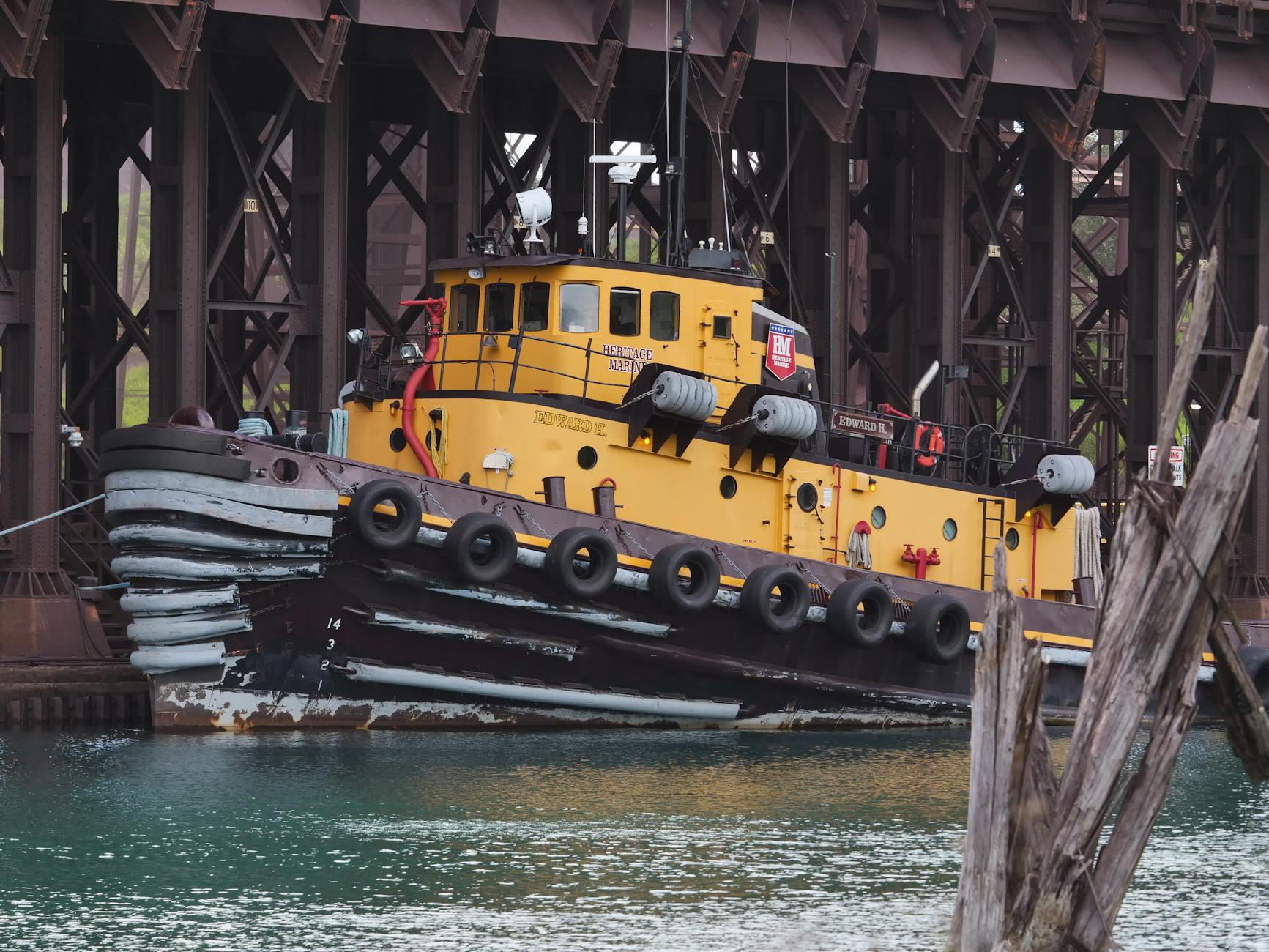 A vintage yellow tugboat docked alongside an industrial structure, showcasing maritime history.